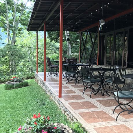Eine überdachte Terrasse mit Sitztischen und Blick in einen grünen Garten