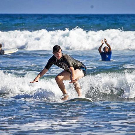 Surfstunde Mann Montezuma Blick auf Mann surfend gen Strand mit Beifall klatschendem Surflehrer im Hintergrund