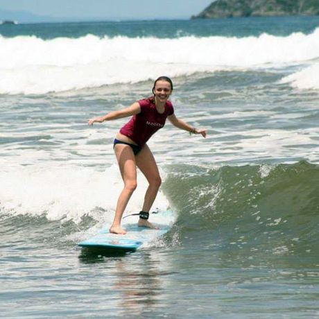 Surfen in Ballena 02 Eine junge Frau surft auf einer Welle und lächelt vor lauter Freude und Spaß über das ganze Gesicht.
